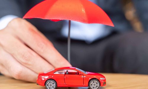 Businessman hand holding umbrella cover or protection red car toy on table. Car insurance concept